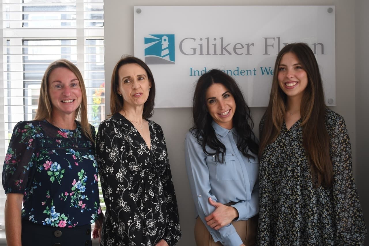 The Giliker Flynn team in front of the company sign in the office